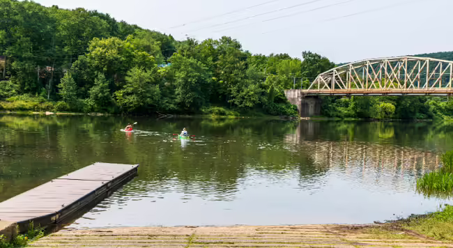 two kayakers paddle away from put-in on a placid river near bridge