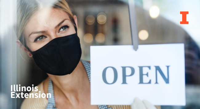 Business owner wearing a mask with an open store sign