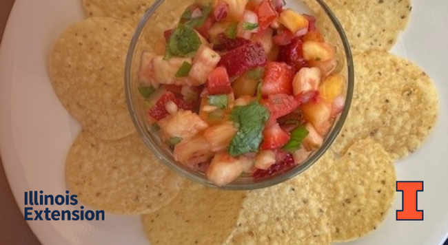Clear bowl with pineapple and strawberry salsa surrounded by tortilla chips on a white plate. Contains orange I block logo and Illinois Extension wordmark.
