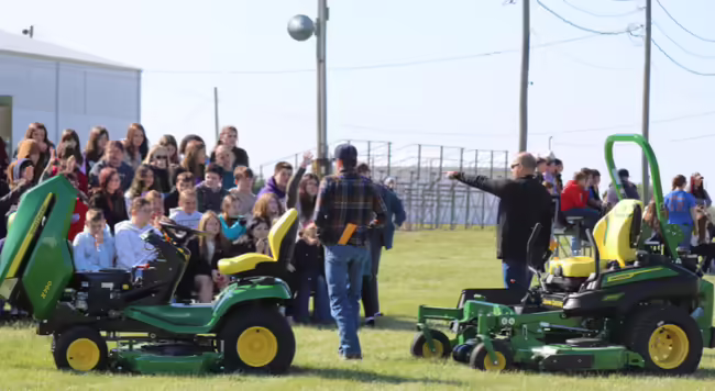 Group of youth sitting outside answering a question pertaining lawn mower safety. 