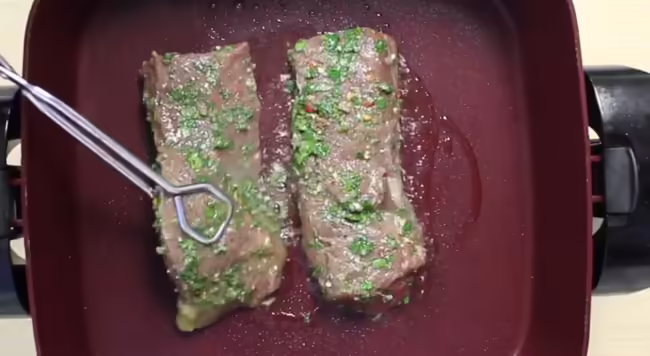 Red nonstick skillet cooking two venison steaks