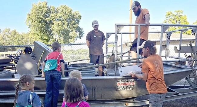 Elementary school children look at boat while adults give lesson about boats