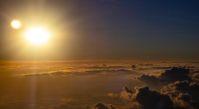 Rays of light from the sun above a layer of clouds over the earth.