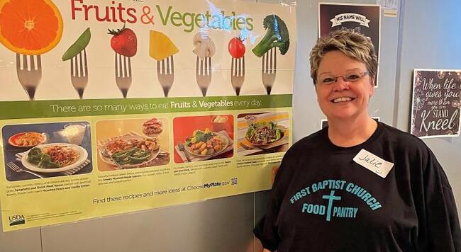 Julie Henderson, new First Baptist Food Pantry manager, with poster on fruits and vegetables