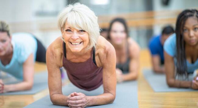 senior woman in purple tank top holds a plank position in a yoga class