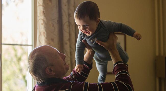 grandfather holding up a smiling infant