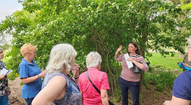 Woman speaking to a group in front of a tree