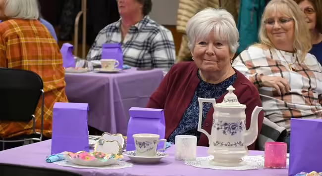 Woman smiling, sitting at a table with a tea pot