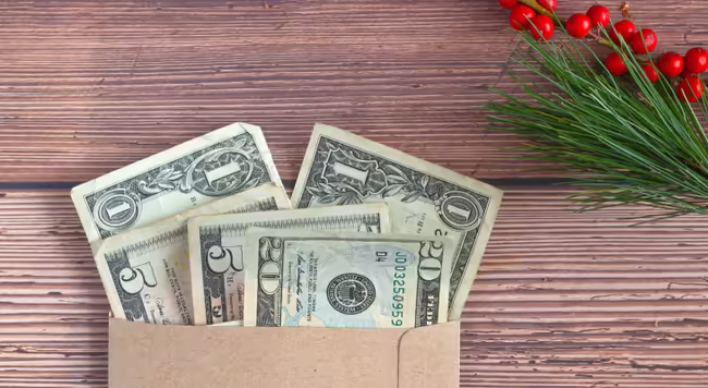 One, five, and twenty dollar bills in an envelope on a table decorated with greenery and red berries.