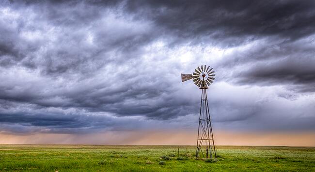 Stormy clouds moving across a windmill in a Midwest pasture. 