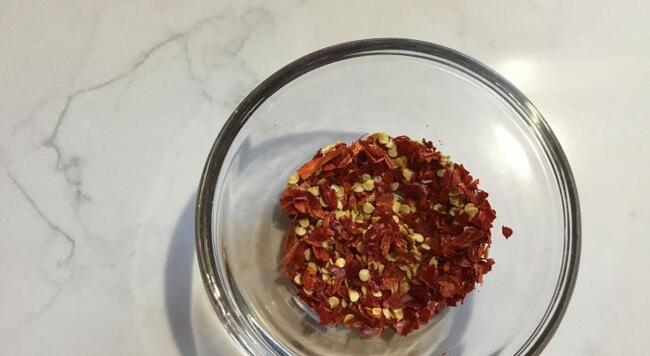 Bowl of red pepper flakes on marble background