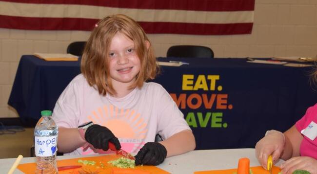 Smiling child learns how to safely cut vegetables at cooking class