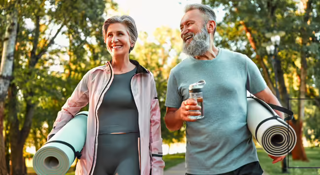 Older woman and man walking holding yoga mats outside