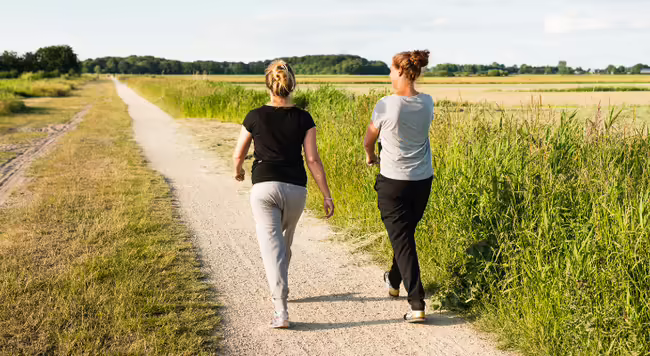 Two people walk on a dirt path through a prairie landscape