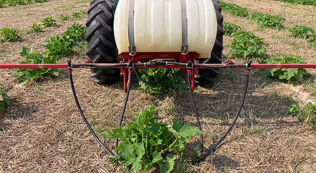 tractor pulling a spray tank with a long bar attached and hoses hanging down to the ground