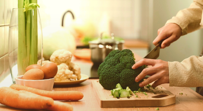 Image of person chopping broccoli on a cutting board in a kitchen