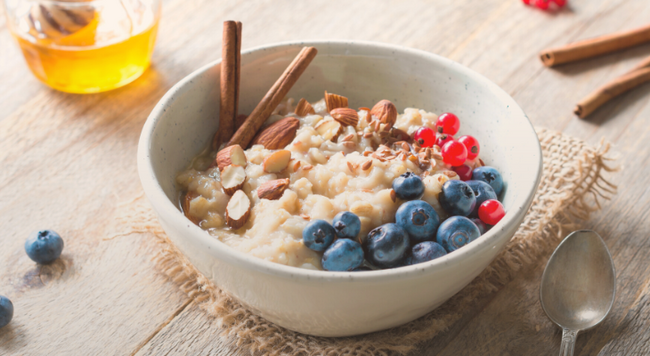 Image of a bowl with oatmeal, blueberries, almonds, and cinnamon on a table with a poon and jar of honey
