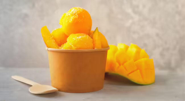 Cup of mango sorbet next to wooden spoon and half of a mango