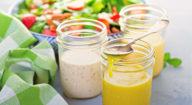 jars of salad dressings and mayonnaise next to a napkin and bowl of salad