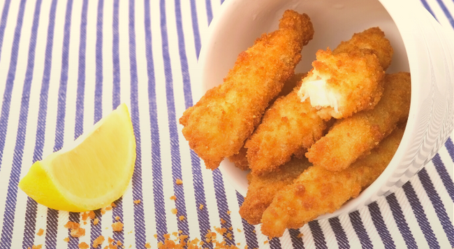 breaded cod fish in a bowl next to a lemon wedge