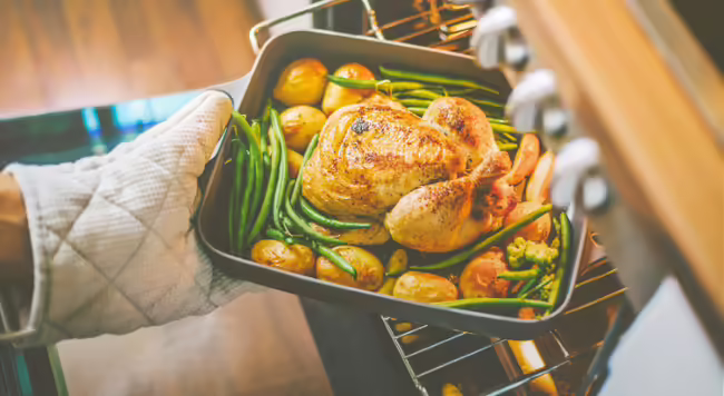 Hand with oven mitt pulling food in pan out of oven