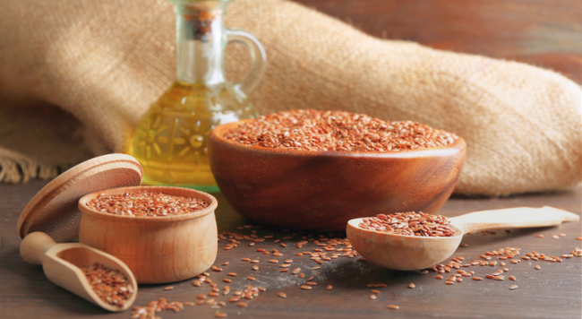 Flaxseed oil next to wooden spoons and bowls filled with flaxseed