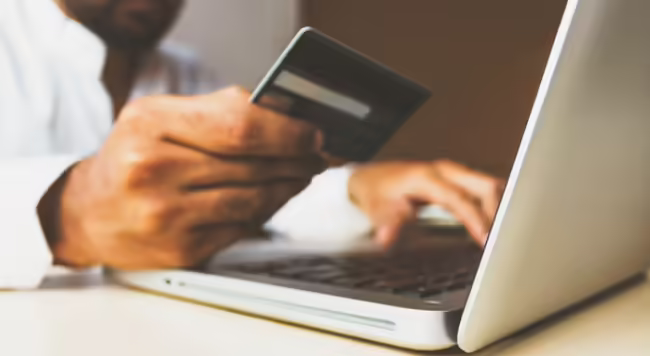 Laptop with hands on the keyboard and holding credit card