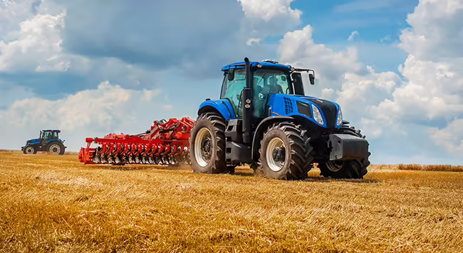 A blue tractor with a red implement in a field. 