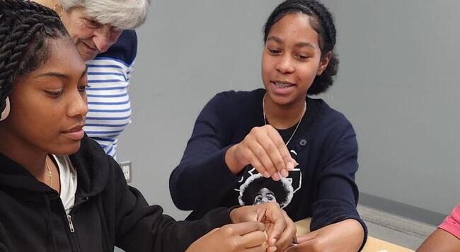 Two teen students work on science project with adult giving instructions