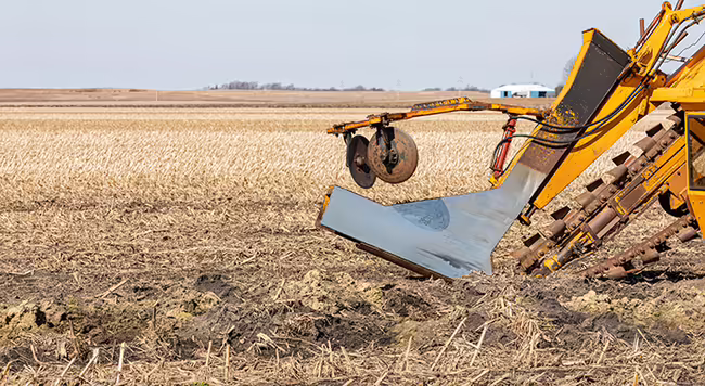 A tile plow attached to a tractor.
