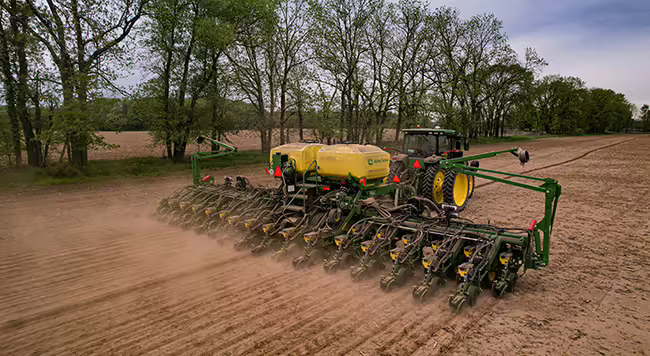 A green tractor pulling a planter across a field. 