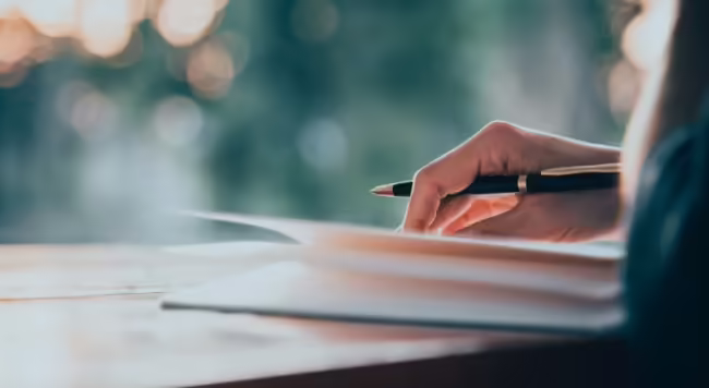 hand holding pen and lightly holding down pages of book