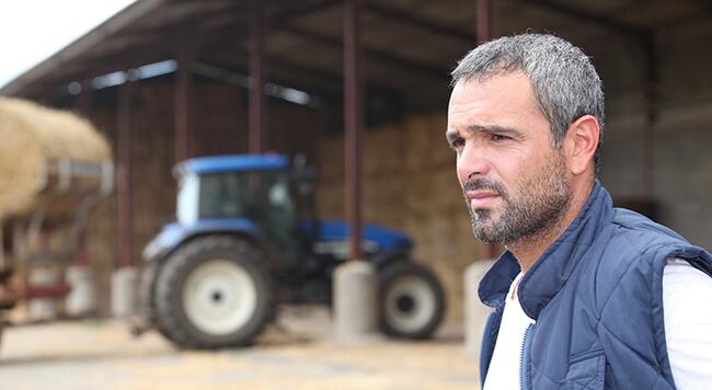 Worried looking middle-aged caucasian male in front of tractor with hay bales