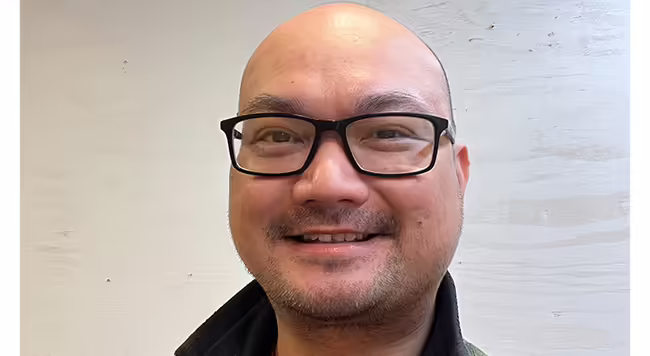 photo of a person smiling with no hair and glasses 
