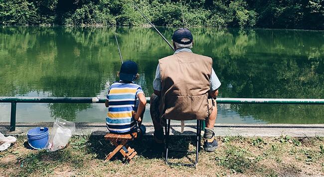 Man and boy fishing together at pond