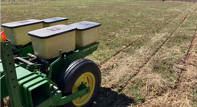 equipment on back of tractor drilling seeds into a field