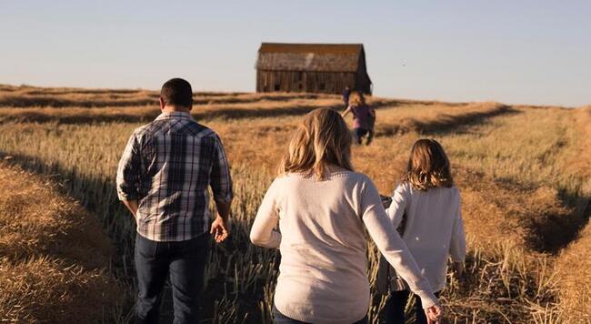 family running through a field toward an old barn