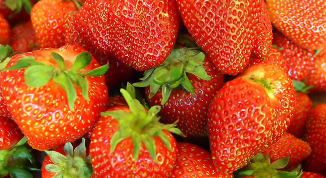 red strawberries with green tops laying on more red strawberries with green tops 