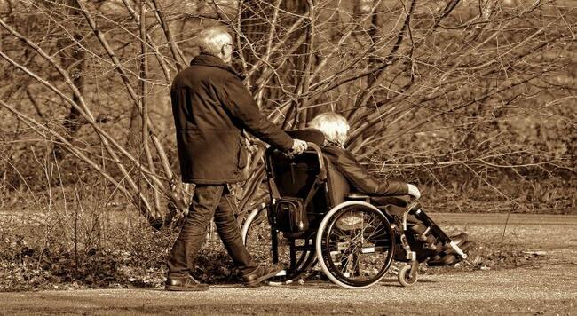 older man pushing older woman in wheelchair