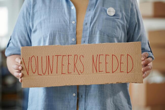 ""person holding cardboard sign that says "volunteers needed"