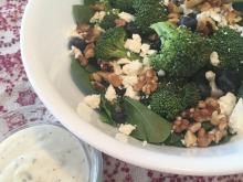 Spinach and broccoli salad with dressing in cup on side