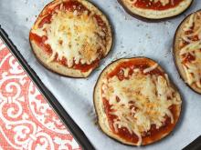 Sliced eggplant topped with tomato sauce and cheese on white plate with pink patterned fabric in background