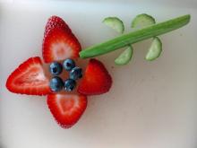 Food flower made with sliced strawberries as petals, blueberries as flower center, and cucumber slices as stem and leaves