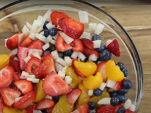 Glass bowl filled with jicama, blueberries, strawberries, mandarin oranges on a wood background