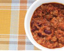 White bowl of chili on yellow and gray plaid placemat