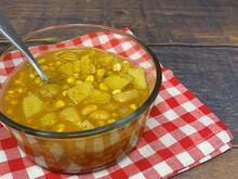 Large glass bowl with chowder and a spoon. Bowl sits on red and white checkered placemat on dark wood background