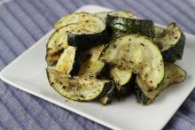 Half moons of seasoned cooked zucchini on white square plate on light blue placemat