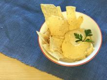 White bowl filled with hummus, tortilla chips, and parsley sitting on blue placemat