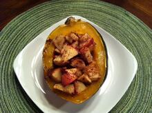 Acorn squash half filled with apples on white square plate and green placemat