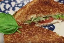 Blue and white plate with sandwich cut in half and garnished with basil leaves